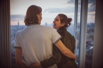 Feliz joven pareja abrazándose en la ventana de rascacielos - foto de stock
