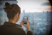 Businesswoman with camera phone photographing sunset over city — Stock Photo