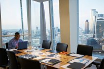 Businessman working at laptop in highrise conference room, London, UK — Stock Photo