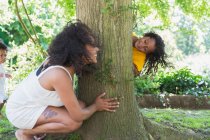 Playful mother and daughter playing hide and go seek at tree — Stock Photo