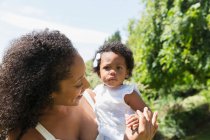 Portrait mother holding cute toddler daughter in sunny garden — Stock Photo