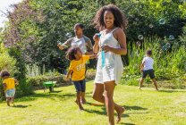 Felice famiglia che gioca e soffia bolle nel soleggiato giardino estivo — Foto stock