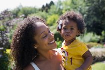 Porträt glückliche Mutter hält süße Kleinkind-Tochter im sonnigen Hof — Stockfoto