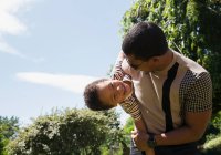 Играющий отец держит счастливого сына на солнечном летнем заднем дворе — стоковое фото