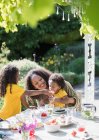 Feliz madre e hijas comiendo en la soleada mesa de jardín de verano - foto de stock