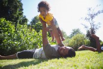 Pai levantando bonito criança filha sobrecarga na grama ensolarada verão — Fotografia de Stock