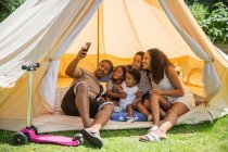 Счастливая семья делает селфи с телефоном внутри летней палатки — стоковое фото