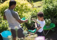 Padre e hijo de jardinería con guantes en el soleado patio de verano - foto de stock