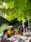 Щаслива сім'я насолоджується обідом за сонячним літнім садовим столом — стокове фото