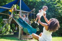 Família feliz jogando no playground definido no quintal ensolarado verão — Fotografia de Stock