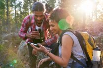Feliz joven pareja de senderismo utilizando el teléfono inteligente en bosques soleados - foto de stock