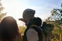 Giovane coppia escursioni e utilizzando il telefono della fotocamera in boschi soleggiati — Foto stock