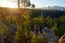 Joven pareja de senderismo relajándose en la roca en bosques pintorescos soleados - foto de stock