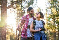 Happy affectionate young couple hiking with camera in sunny woods — Stock Photo