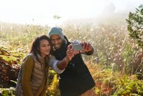 Feliz joven pareja con cámara de teléfono tomando selfie en la hierba alta soleado - foto de stock