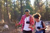 Happy young couple hiking with binoculars and camera in sunny woods — Stock Photo