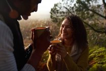 Счастливая молодая пара пьет кофе в солнечном лесу — стоковое фото