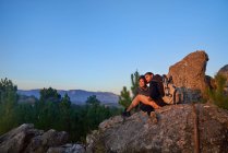 Молода пара туристів розслабляється на скелі і насолоджується заходом сонця — стокове фото