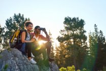 Young couple hiking with binoculars on rocks in sunny woods — Stock Photo