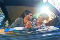 Joyeux jeune couple relaxant à l'arrière de la voiture ensoleillée — Photo de stock