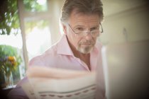 Senior liest Zeitung am Laptop in sonniger Morgenküche — Stockfoto