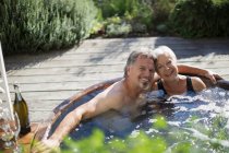 Retrato casal sênior feliz relaxando na banheira de hidromassagem no pátio ensolarado — Fotografia de Stock