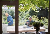 La jardinería de pareja mayor y el uso de tabletas digitales en el soleado patio de verano - foto de stock