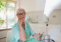 Portrait confident senior woman using smart phone in morning kitchen — Stock Photo