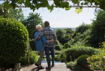 Ласковая пожилая пара обнимается на солнечном патио летнего сада — стоковое фото