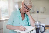 Femme âgée écrivant dans un journal à la cuisine du matin — Photo de stock