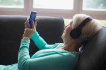 Donna anziana rilassante con cuffie e smartphone sul divano — Foto stock