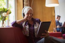 Happy senior woman using headphones and digital tablet on sofa — Stock Photo