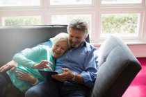 Happy senior couple cuddling and using digital tablet on sofa — Stock Photo
