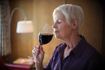 Serena donna anziana odore e degustazione di vino rosso — Foto stock