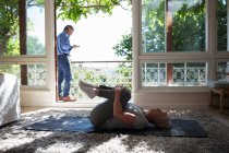Senior woman stretching on yoga mat at summer balcony doorway — Stock Photo