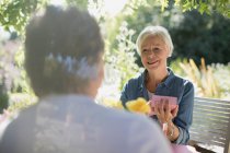 Счастливая пожилая женщина открывает подарок от мужа на солнечном летнем дворике — стоковое фото