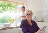 Portrait happy senior woman using smart phone in sunny kitchen — Stock Photo