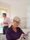 Mujer mayor usando teléfono inteligente en la cocina - foto de stock