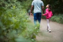 Father and daughter holding hands hiking on path in woods — Stock Photo