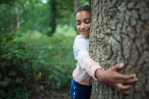 Bonito menina abraçando árvore tronco no madeiras — Fotografia de Stock