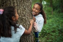 Happy sisters playing at tree trunk in woods — Stock Photo