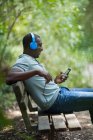Чоловік слухає музику з навушниками та смартфоном на лавці парку — стокове фото