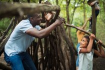 Père et fille construisant un tipi avec des branches dans les bois — Photo de stock