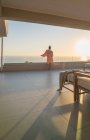 Жінка в халаті насолоджується видом на океан на захід сонця з розкішного балкона — стокове фото