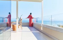 Femme en robe profitant d'une vue panoramique ensoleillée sur l'océan depuis le balcon de luxe — Photo de stock