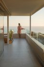 Женщина расслабляется с белым вином на роскошном балконе с видом на океан — стоковое фото