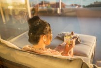 Frau entspannt sich mit Wasser auf sonnigem Terrassensofa — Stockfoto