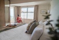 Frau liest Buch am sonnigen Morgenfenster im Luxusschlafzimmer — Stockfoto