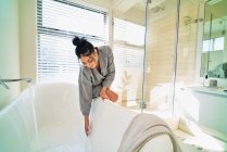 Donna in bagno preparare vasca da bagno per il bagno in camera da letto soleggiata — Foto stock