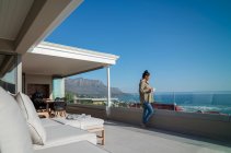 Frau genießt Kaffee auf sonnigem Luxus-Balkon mit Meerblick — Stockfoto